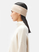 A model is wearing beige cashmere ribbed knit headband with a small white rectangular brand tag, displayed flat against a light gray background. #color_beige