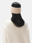 A model is wearing beige cashmere ribbed knit headband with a small white rectangular brand tag, displayed flat against a light gray background. #color_beige
