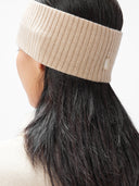 A model is wearing beige cashmere ribbed knit headband with a small white rectangular brand tag, displayed flat against a light gray background. #color_beige