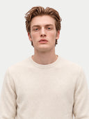 A young man with light brown hair wearing a cream-colored knit crewneck sweater, photographed against a solid light gray background.