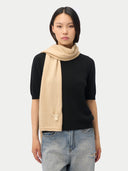 A model wearing a black short-sleeve knit sweater and light blue jeans, styled with a beige knit scarf draped over the shoulder, against a light gray studio background.