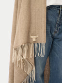 A close-up of a beige and cream herringbone patterned scarf with fringe, draped over blue jeans against a light gray background. #color_off-white