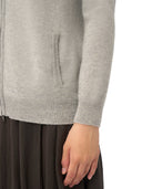 Close-up of a person wearing a light gray knit zip-up cardigan with a ribbed hem and sleeve cuffs, paired with a dark brown skirt, against a plain white background.
