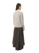 A woman shown from the back wearing a light gray knit mock-neck sweater and a dark brown high-low midi skirt, paired with black flat shoes, against a plain white background.