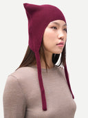 Model wearing a maroon knitted hat with long ear flaps on a plain background. #color_deep-wine