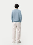 Person wearing a light blue cashmere sweater and white pants on a white background. #color_light-blue