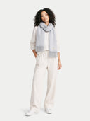 Woman wearing a light gray scarf and white pants on a white background