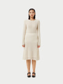A woman wearing a beige knit cashmere skirt with an elasticated high-waist, paired with a white blouse with a sleeve detail.  #color_off-white
