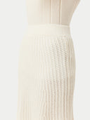 A woman wearing a beige knit cashmere skirt with an elasticated high-waist, paired with a white blouse with a sleeve detail.  #color_off-white