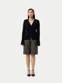A woman wearing a black cashmere v-neck buttoned cardigan over a cashmere top and shorts. #color_black