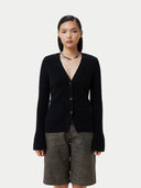 A woman wearing a black cashmere v-neck buttoned cardigan over a cashmere top and shorts. #color_black