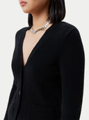 A woman wearing a black cashmere v-neck buttoned cardigan over a cashmere top and shorts. #color_black
