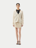 A woman wearing a beige cotton cashmere cardigan with a crew neckline and button closures over a black top and a beige skirt. #color_pure-white