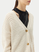 A woman wearing a beige cotton cashmere cardigan with a crew neckline and button closures over a black top and a beige skirt. #color_pure-white