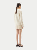 A woman wearing a beige cotton cashmere cardigan with a crew neckline and button closures over a black top and a beige skirt. #color_pure-white