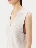 Woman wearing a light pink sleeveless cashmere top and white pants on a white background. #color_pure-white