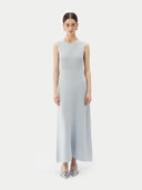 A woman standing in a studio setting, wearing a sleeveless, solid blue cashmere dress with a round neckline. #color_soft-ice