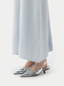 A woman standing in a studio setting, wearing a sleeveless, solid blue cashmere dress with a round neckline. #color_soft-ice