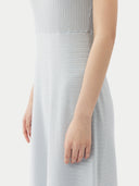 A woman standing in a studio setting, wearing a sleeveless, solid blue cashmere dress with a round neckline. #color_soft-ice