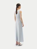 A woman standing in a studio setting, wearing a sleeveless, solid blue cashmere dress with a round neckline. #color_soft-ice