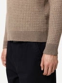 Close-up of a person wearing a brown textured cashmere sweater and black pants on a white background. #color_taupe
