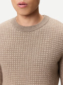Close-up of a person wearing a beige textured cashmere sweater against a neutral background. #color_taupe