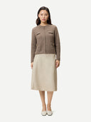 A woman modeling a cropped, textured knit cardigan in taupe brown with front flap pockets and a central zipper, paired with a light beige skirt, against a plain light gray background. #color_taupe