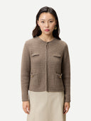 A woman modeling a cropped, textured knit cardigan in taupe brown with front flap pockets and a central zipper, paired with a light beige skirt, against a plain light gray background. #color_taupe