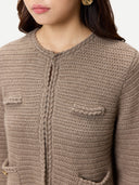 A woman modeling a cropped, textured knit cardigan in taupe brown with front flap pockets and a central zipper, paired with a light beige skirt, against a plain light gray background. #color_taupe