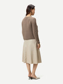 A woman modeling a cropped, textured knit cardigan in taupe brown with front flap pockets and a central zipper, paired with a light beige skirt, against a plain light gray background. #color_taupe