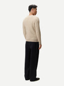 Man wearing a beige cashmere sweater and black pants on a white background.  #color_dusty-beige