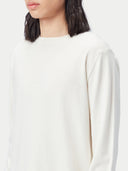 A long-sleeve crewneck knit cashmere sweater in a warm off-white or cream color, displayed flat against a light gray background. #color_pure-white