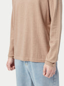 Person wearing a beige cashmere sweater and light blue jeans on a white background #color_taupe-brown