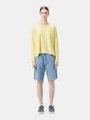 A woman wearing a yellow boatneck cotton silk cashmere blend sweater with long sleeves, paired with blue denim pants. #color_green-sheen