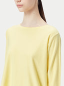A woman wearing a yellow boatneck cotton silk cashmere blend sweater with long sleeves, paired with blue denim pants. #color_green-sheen