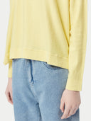 A woman wearing a yellow boatneck cotton silk cashmere blend sweater with long sleeves, paired with blue denim pants. #color_green-sheen
