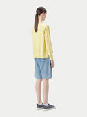 A woman wearing a yellow boatneck cotton silk cashmere blend sweater with long sleeves, paired with blue denim pants. #color_green-sheen