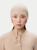 Woman wearing a beige knitted hat with tassels on a white background