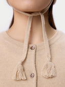 Close-up of a beige cardigan with tassel details on a plain background
