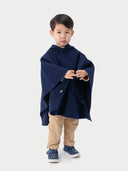 A child wearing a navy hooded cashmere poncho with a plain background. #color_navy-blue