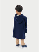 A child wearing a navy hooded cashmere poncho with a plain background. #color_navy-blue