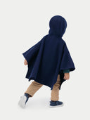 A child wearing a navy hooded cashmere poncho with a plain background. #color_navy-blue
