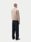 A man wearing a light beige cashmere utility jacket with a collar, front button closure, and two large flap chest pockets, layered over a white collared shirt and dark trousers, against a plain light gray studio background. #color_taupe