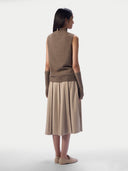 A model shown from the back wearing a sleeveless taupe-brown knit mock-neck sweater vest with matching ribbed cuffs, paired with a pleated beige midi skirt and beige loafers, against a light gray studio background.
