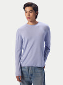 A man wearing a light blue crewneck knit sweater with a rolled neckline and light-wash blue jeans, standing against a light gray studio background.