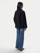 A model shown from the back wearing a black oversized jacket and wide-leg blue jeans against a plain light gray studio background.