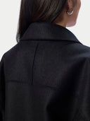 A model shown from the back wearing a black oversized jacket and wide-leg blue jeans against a plain light gray studio background.