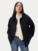 A model shown from the back wearing a black oversized jacket and wide-leg blue jeans against a plain light gray studio background.