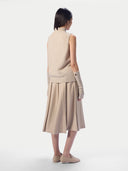A model shown from the back wearing a beige knit sleeveless vest over a matching beige pleated midi skirt, paired with beige knit fingerless gloves and beige flats, against a light gray studio background.