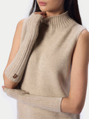 A close-up of a model wearing a sleeveless ribbed knit sweater vest in a light beige color, paired with matching ribbed knit arm warmers.